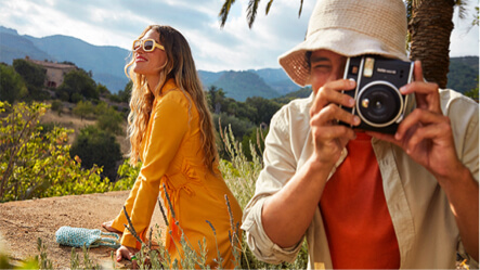 A young man takes a photograph on a tropical mountain next to a young woman taking in the sun