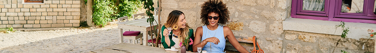 Two women sitting at an outdoor café, smiling and enjoying drinks together.