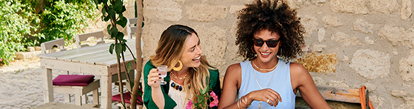 Two women sitting at an outdoor café, smiling and enjoying drinks together.