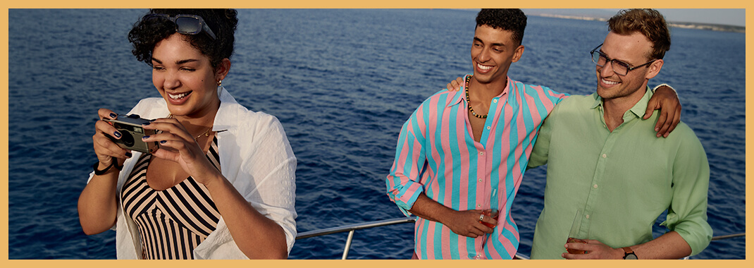 Three friends on a boat, one taking a photo while the other two smile and pose together with the ocean in the background.