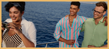 Three friends on a boat, one taking a photo while the other two smile and pose together with the ocean in the background.