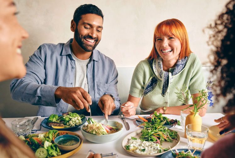 Group of four adults smiling and enjoying a meal together at a table