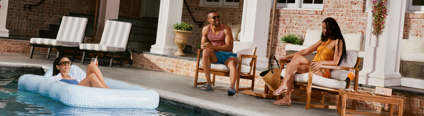 A man and woman sitting in chairs under umbrella by a pool.