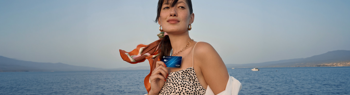 Woman holding a Sapphire Preferred credit card while standing outdoors by the water.