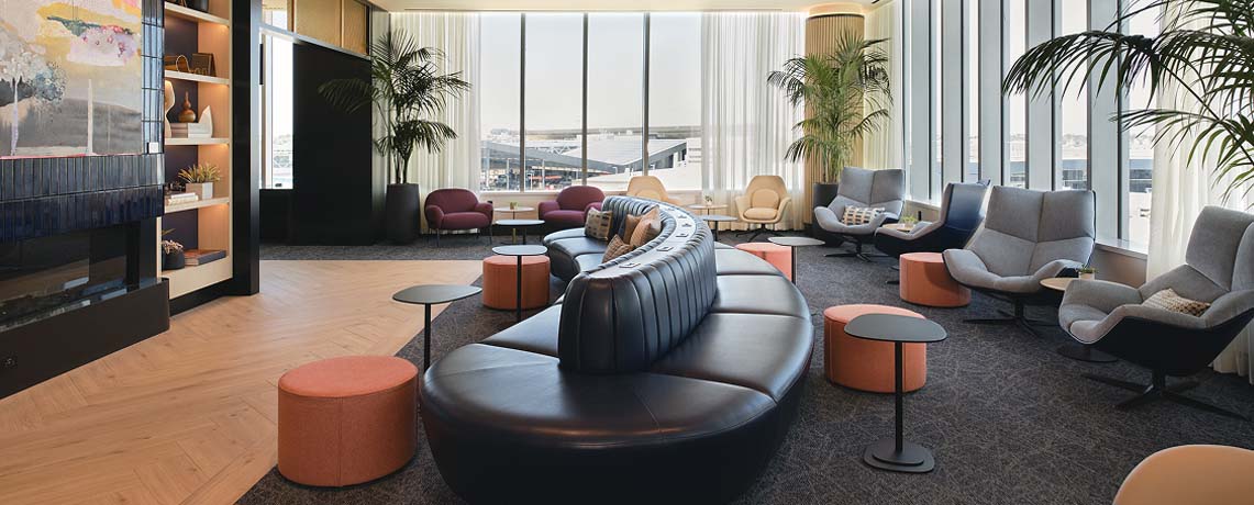 Modern Sapphire Lounge at Boston Logan International Airport with curved leather sofas, armchairs, small tables, and large windows with runway views.