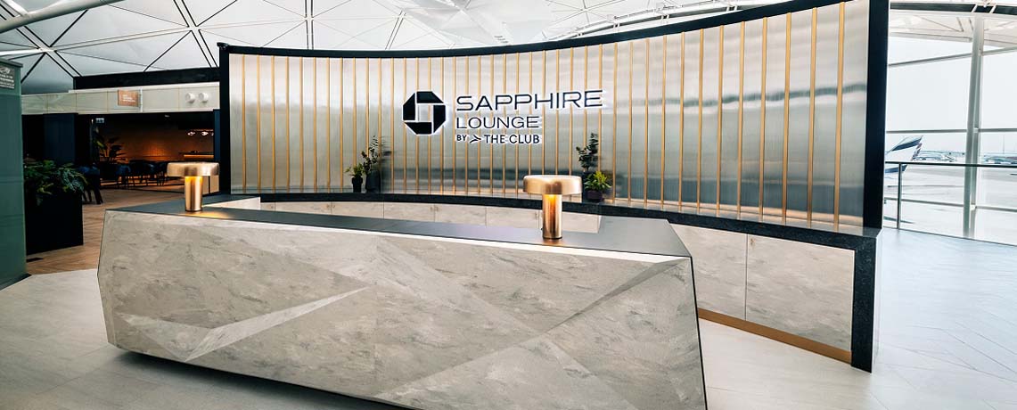 Reception area of the Sapphire Lounge at Hong Kong International Airport with a sleek stone desk, gold bars, and the lounge logo.